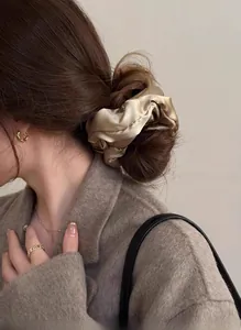 Detail of a large champagne gold satin silk scrunchie styled on a woman's hair bun