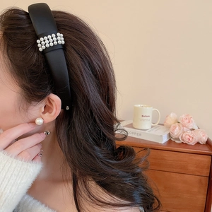 Detail of elegant black satin headband with white pearls on a model in a warm indoor setting