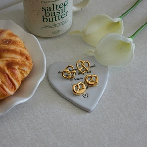 Close-up of gold pretzel heart earrings on a white heart ceramic tray with calla lilies