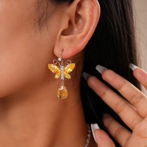 Close-up of a model wearing yellow butterfly earrings with teardrop pendants