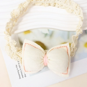 Detailed close-up of a cream baby headband with a handmade fabric bow and lace strap