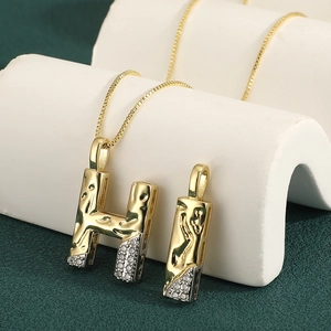 Macro shot of HI letter pendants with pavé zircons and textured lava gold finish