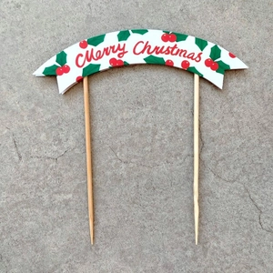 Detail of Merry Christmas cake topper featuring red lettering and green leaves with wooden sticks