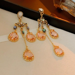Macro detail of gold vintage earrings featuring peach crystal teardrops and tassel chain