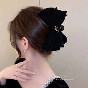 Detail of elegant black velvet bow hair claw with gold metal logo on a model