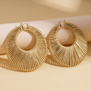 Macro detail of gold-finish woven hollow geometric hoop earrings with radial sunburst texture
