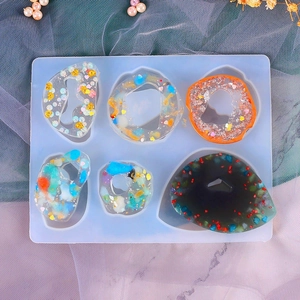 Flat lay of geometric silicone molds for resin pendants on gray gauze with pearls