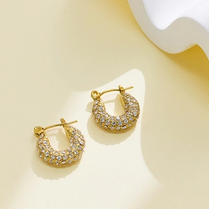 Macro detail of gold C-shaped hoop earrings with pave white crystal stones