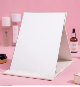 Close-up of portable white folding mirror with premium leather texture on pink background