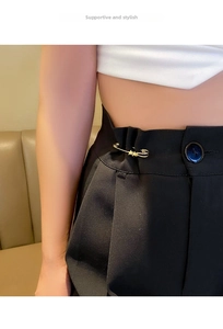 Detail of gold metal safety pin with stars used as waist tightener on black pants