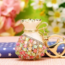 Detail of money bag keychain featuring cream enamel finish and vibrant gemstone inlay