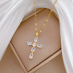 Détail du pendentif croix dorée avec cristaux sur fond de soie blanche