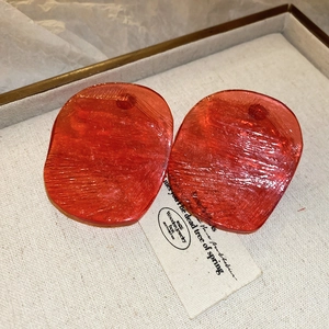 Macro shot of red irregular resin earrings with silver needles and textured surface