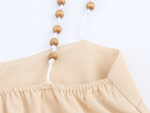 Detail der Holzperlen und weißen Flechtseile an einem beigen Bohemian-Kleid
