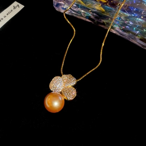 Macro view of gold-plated flower pendant with a golden pearl on a fine snake chain