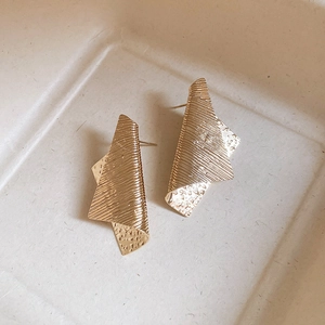 Detail of golden irregular geometric earrings with combined brushed and hammered textures