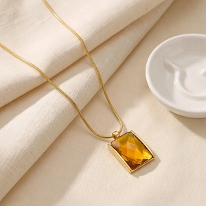 Close-up of a square amber glass pendant on a gold 18K plated snake chain necklace