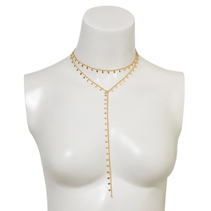 Detail view of a layered gold Y-necklace with small metallic drop charms on a white bust