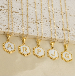 Detail of 18K gold hexagonal initial necklaces with white enamel inlay and silk background