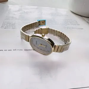 Close-up of golden oval watch with shell dial and crystals on white book pages