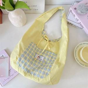 Detail of light yellow canvas tote bag featuring a blue plaid pocket and cartoon label
