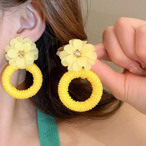 Detail of flower stud earring with resin petals and yellow woven ring pendant on model