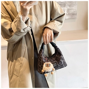 Detail of leopard print handbag with plush cartoon pendant held by model in trench coat