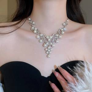 Detail view of a luxury pearl and diamond necklace on a model in a black dress