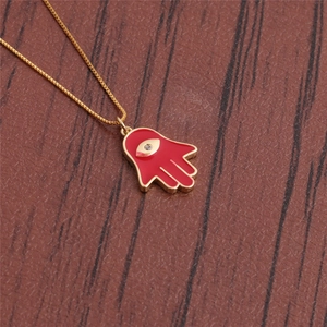 Close-up of golden Hamsa hand pendant with red enamel and crystal evil eye detail