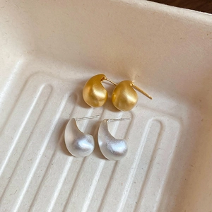 Detail of matte brushed gold and silver teardrop earrings on a textured tray