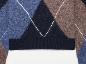 Close-up of diamond pattern knit sweater with ribbed hem and navy blue wool texture