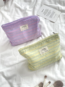 Detail view of striped canvas makeup bags in purple and green on a soft fabric background