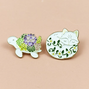 Close-up of enamel turtle with succulents and sleeping fox with flowers lapel pins