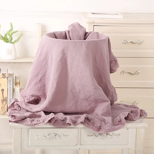 Soft muslin cotton baby blanket in lotus purple with ruffled edges on a white stool