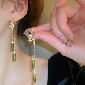 Close-up of golden bamboo tassel earrings with emerald green accents and white beads