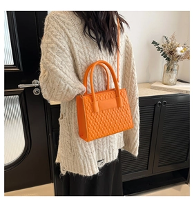 Close-up of orange quilted handbag with elegant shoulder strap on a beige knit sweater