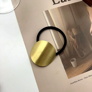 Detail of minimalist golden metal hair tie with brushed texture and black elastic band