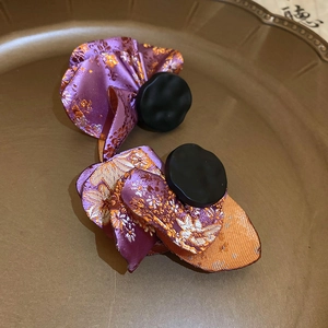Macro detail of pleated purple brocade floral earrings with black round center decoration