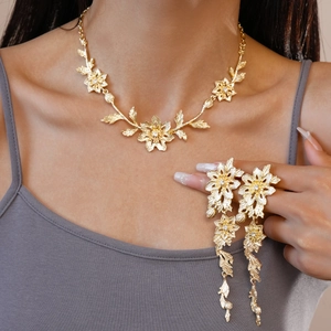 Golden flower leaf necklace and earrings jewelry set worn by a model on a grey top