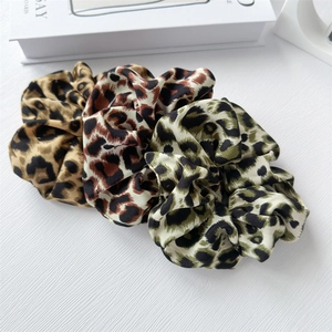 Detailed view of three leopard print scrunchies in brown, red, and grey satin fabric