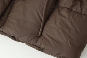 Détail d'une doudoune matelassée marron foncé avec tissu lisse et cordon de serrage