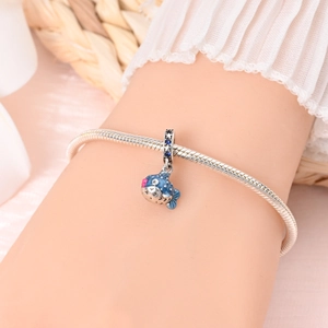 Gros plan d'une breloque poisson-globe en argent et émail bleu sur un bracelet