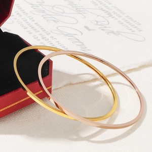 Close-up of thin 18K gold and rose gold stainless steel bangles on a luxury red gift box