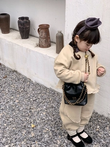Detail eines beigen Kinder-Trainingsanzugs mit schwarzer Kunstleder-Umhängetasche mit Goldkette