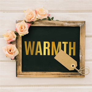 Detail of wooden chalkboard with gold 'WARMTH' letters and pink rose floral decoration