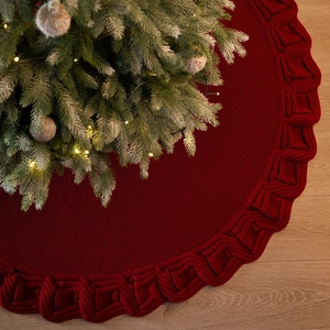 Knitted dark red Christmas tree skirt with thick cable weave border on light wood floor