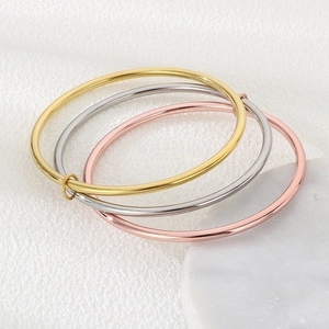Close-up of three interlocking bangles in gold, silver, and rose gold on marble