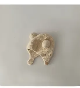 Detail of baby plush earflap hat with wood button and fuzzy pom-poms in beige