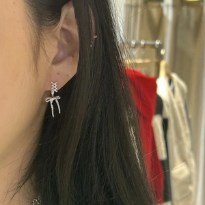 Close-up of a silver bow knot earring worn by a model in a casual indoor setting