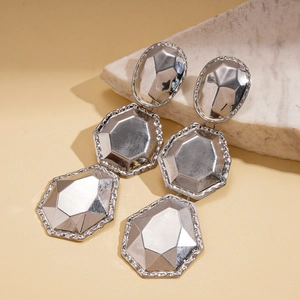 Macro detail of silver geometric faceted drop earrings on white stone display